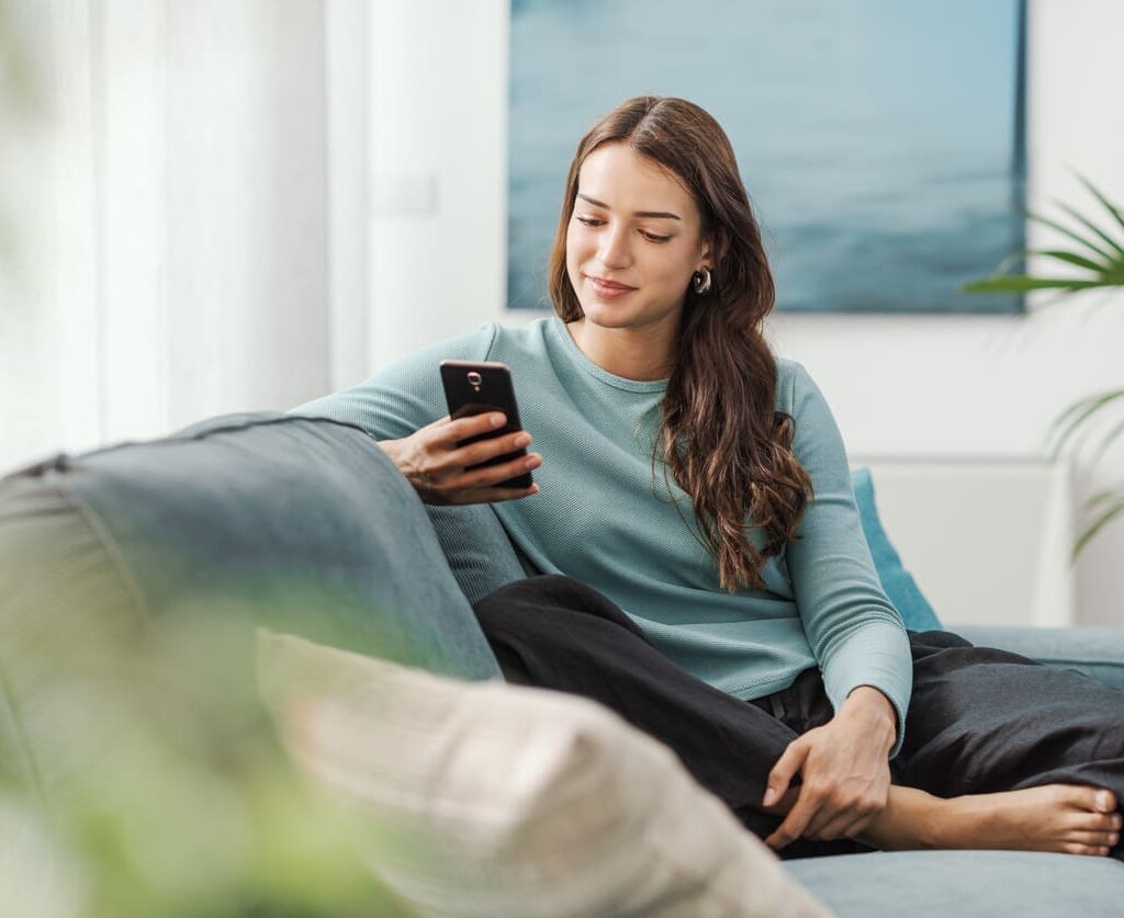 Sieviete skatās telefonu dīvānā